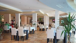 Un amplio comedor interior con varias mesas y sillas, suelo de baldosas y varias plantas en macetas.