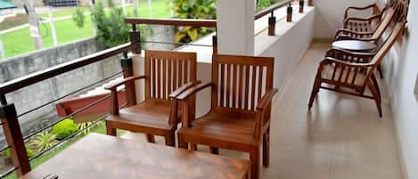 Un balcón con mobiliario de madera, incluyendo sillas y una mesa, con vista a un jardín y un edificio.