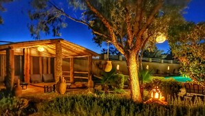 Una cabaña rústica con un porche cubierto, piscina y un gran árbol.