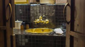 Un baño con pared de azulejos negros, un lavamanos dorado y una puerta de madera.
