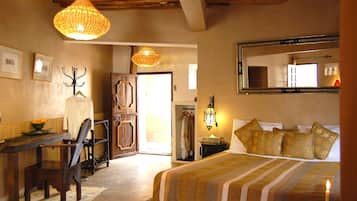 A bedroom with a bed, a desk, a chair, a hanging light fixture, and a mirror on the wall.