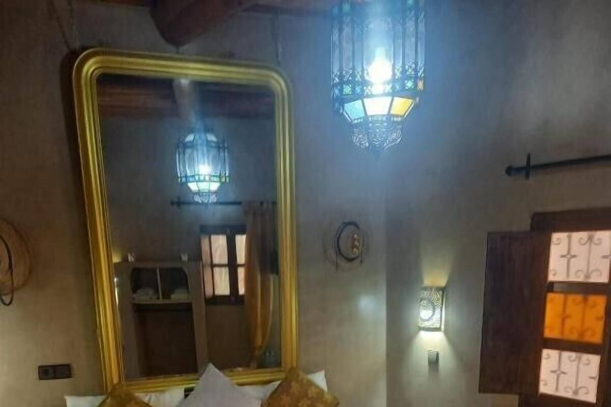 Ett hotellrum med en stor säng, en spegel, en väggmonterad lampa och ett fönster med gardiner.