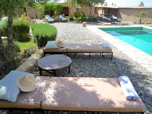 A poolside area with lounge chairs, a small round table, and a pool. - Les Jardins de Skoura (Skoura)
