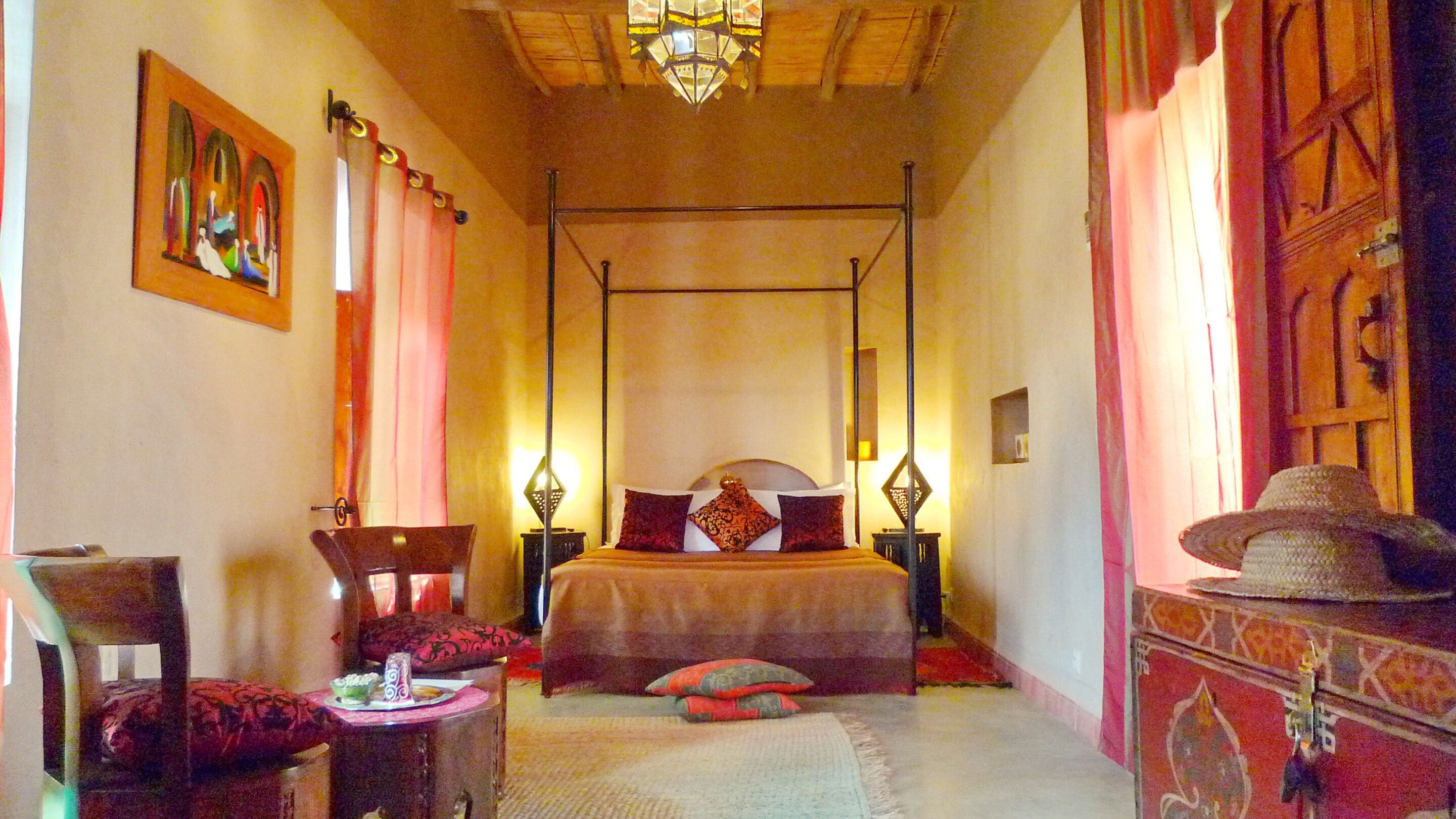 A four-poster bed with a canopy, a side table with a lamp, a chair, and a decorative hat on a stand.