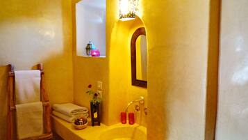 Un baño con un lavamanos amarillo, un espejo, un perchero y un estante pequeño con una vela y una botella.