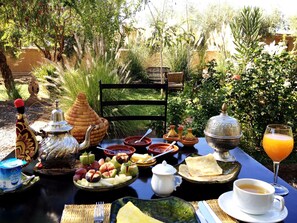 A table set outdoors with various dishes, a teapot, a jug, and a glass of orange juice. - Les Jardins de Skoura (Skoura)