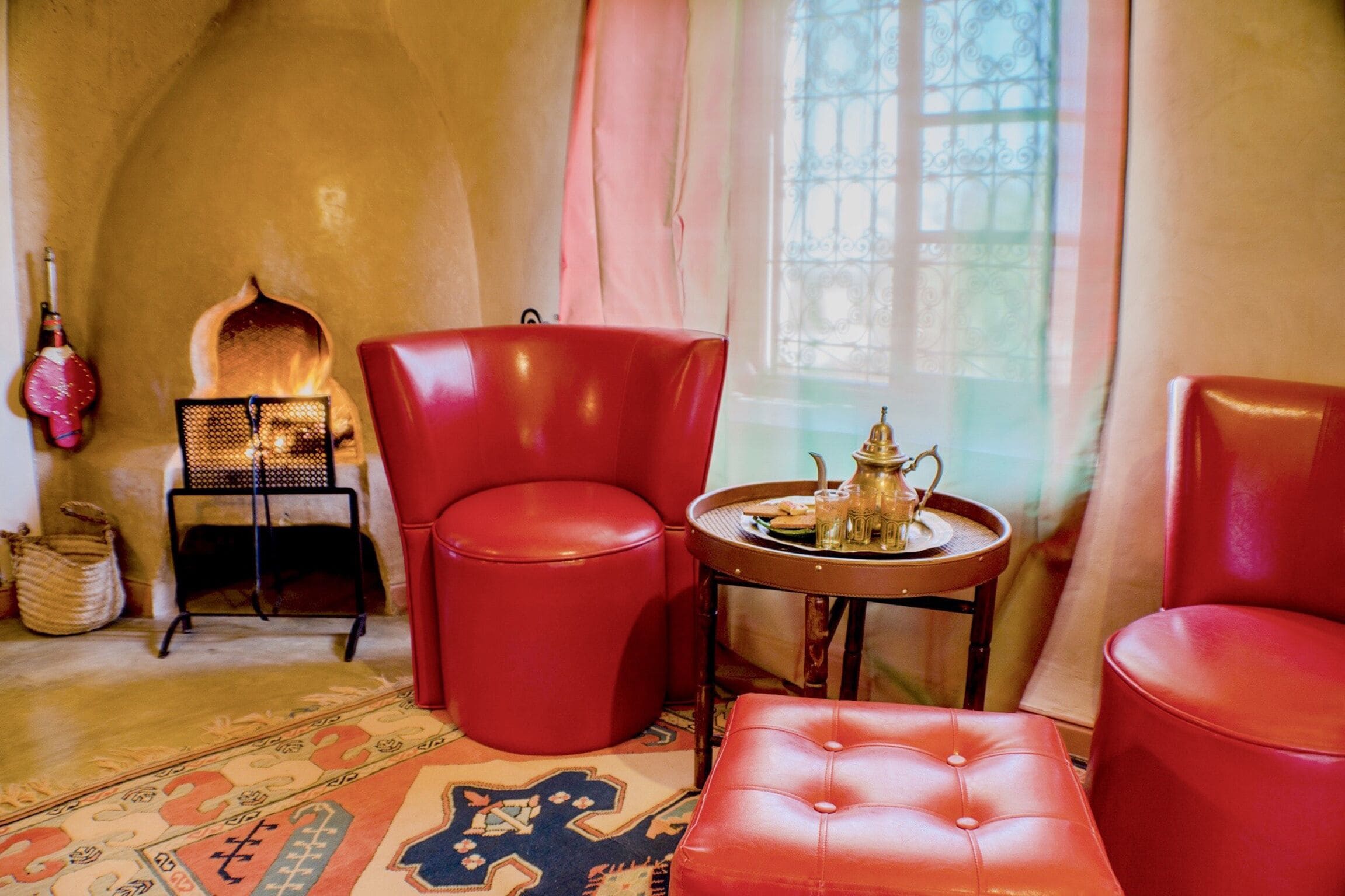 Una habitación acogedora con chimenea, sillones de cuero rojo, un tapete estampado y una mesita con tetera.
