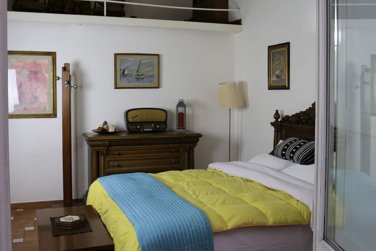 A bedroom with a bed, a dresser, a lamp, and a painting on the wall.