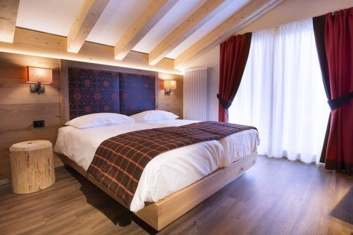 A wooden-framed bedroom with a large bed, two wall-mounted lamps, and a window with red curtains.