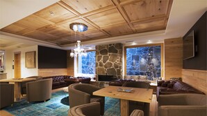 A modern living room with a stone wall, leather sofas, wooden ceiling, and a chandelier. - Chalet Marcora (Campitello di Fassa)