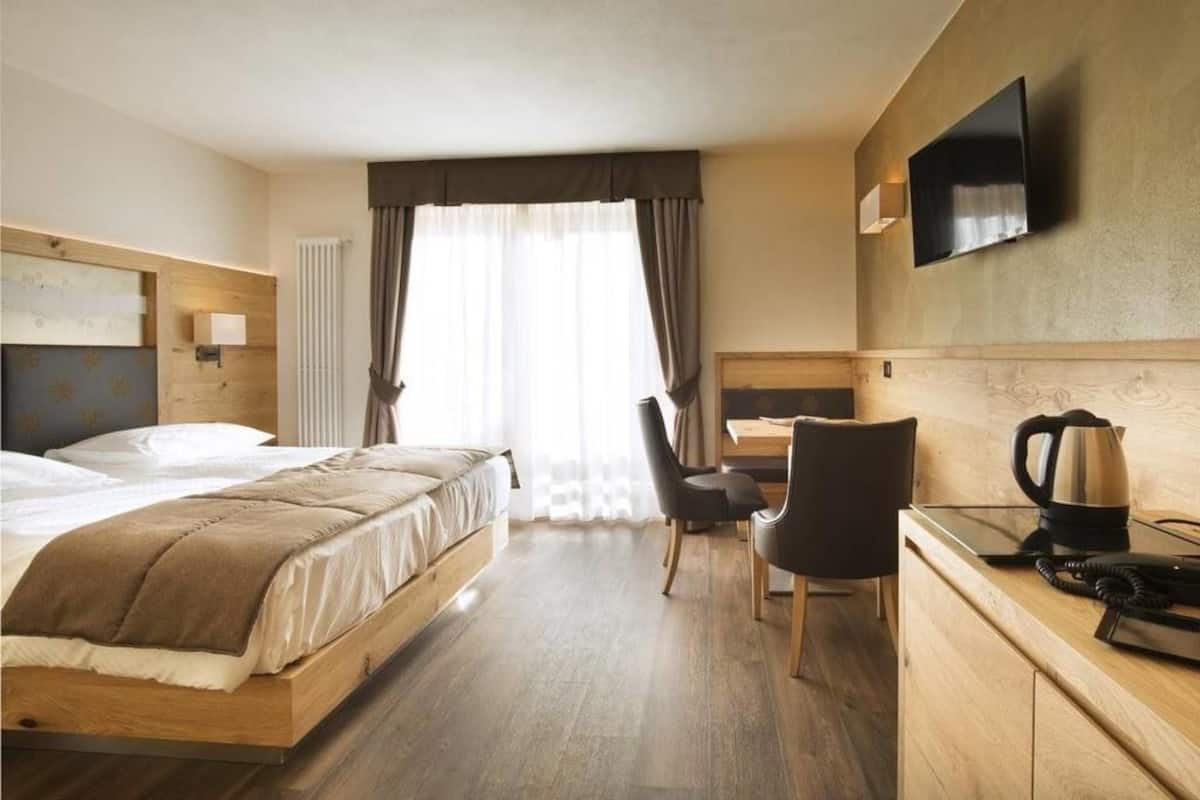 A hotel room with a bed, a desk, a chair, a TV, and a kettle.