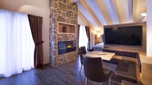 A modern living room with a stone fireplace, a large flat-screen TV, and a cozy seating area. - Chalet Marcora (Campitello di Fassa)