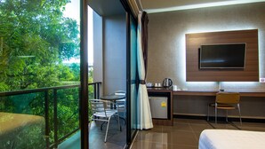 A hotel room with a bed, a desk, a chair, a TV, and a balcony with a view of trees. - PSG Hotel (Udon Thani)