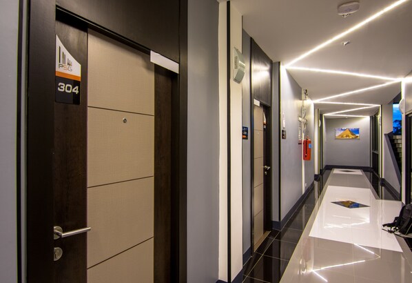 Un pasillo moderno de hotel con piso pulido, un extintor y una puerta marcada con la inscripción 'PSG 304'.
