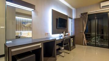 Una habitación de hotel moderna con un escritorio grande, un televisor de pantalla plana, un espejo y una puerta de cristal corredera que da a un balcón.