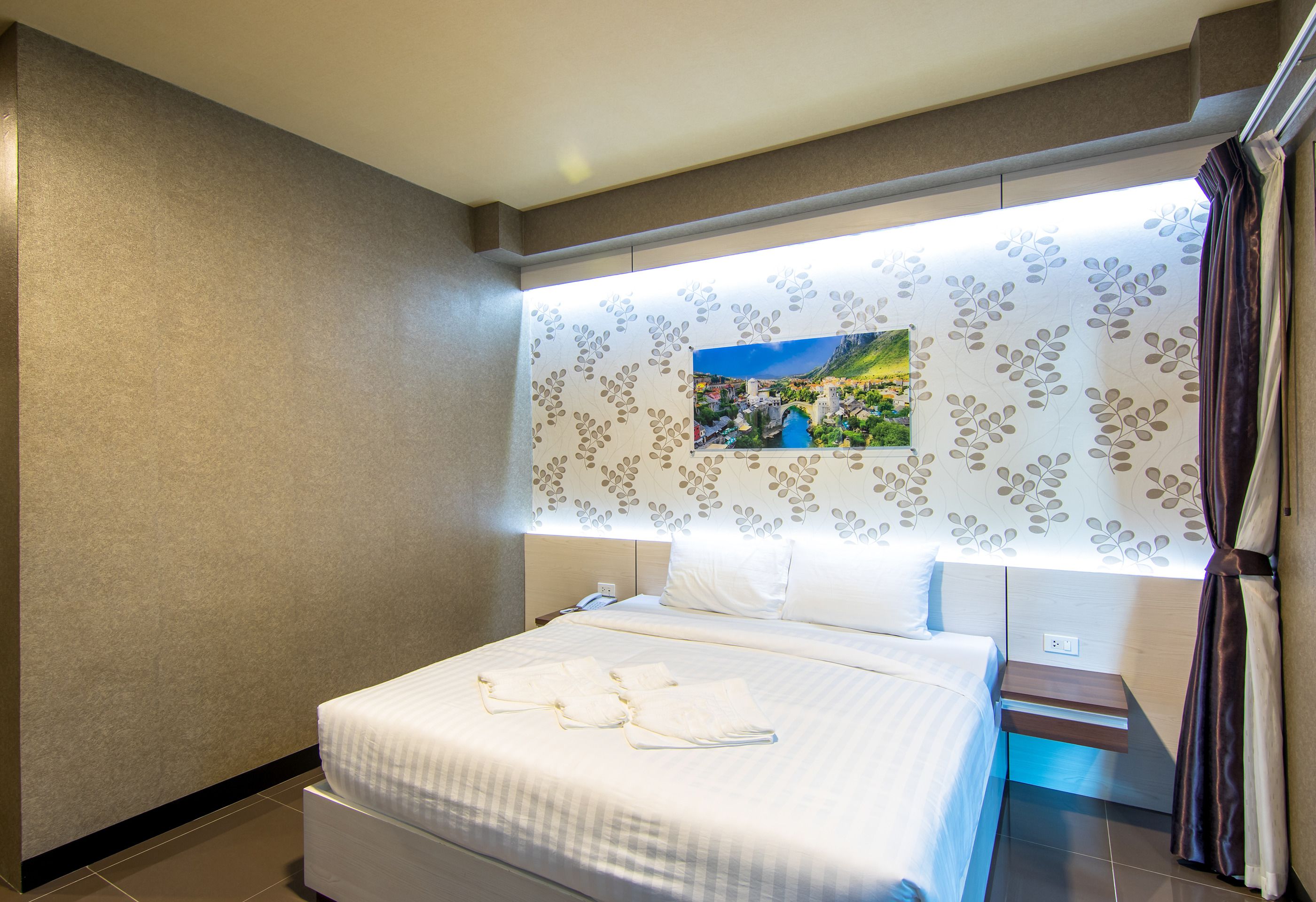 Habitació d'hotel amb llit, una tauleta de nit, televisió penjada a la paret i una finestra amb cortines.