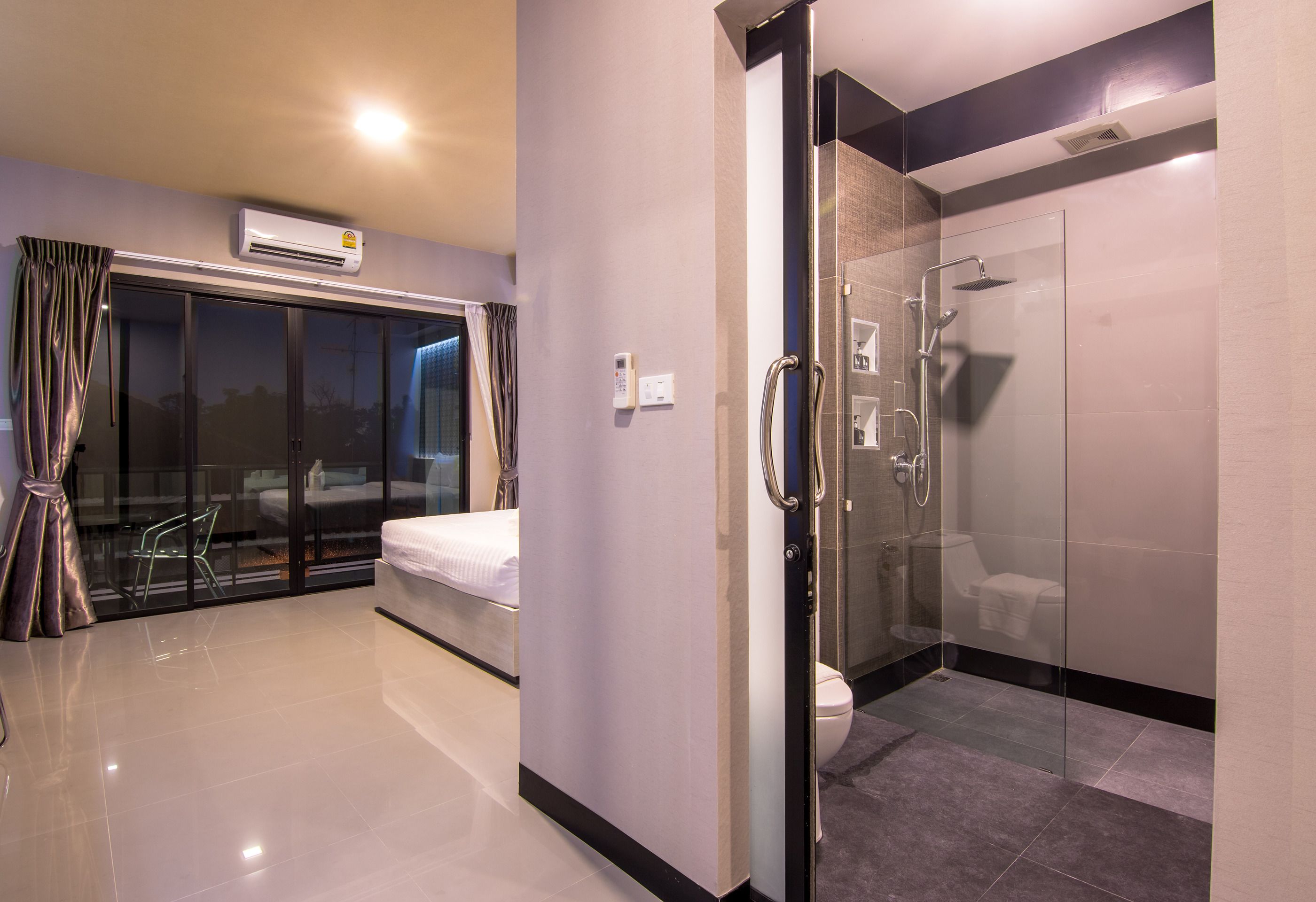 Una habitación de hotel moderna con cabina de ducha de vidrio, una cama, un panel de control y vistas al exterior.