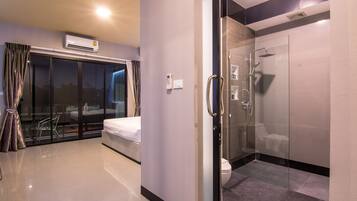 Una habitación de hotel moderna con cabina de ducha de vidrio, una cama, un panel de control y vistas al exterior.