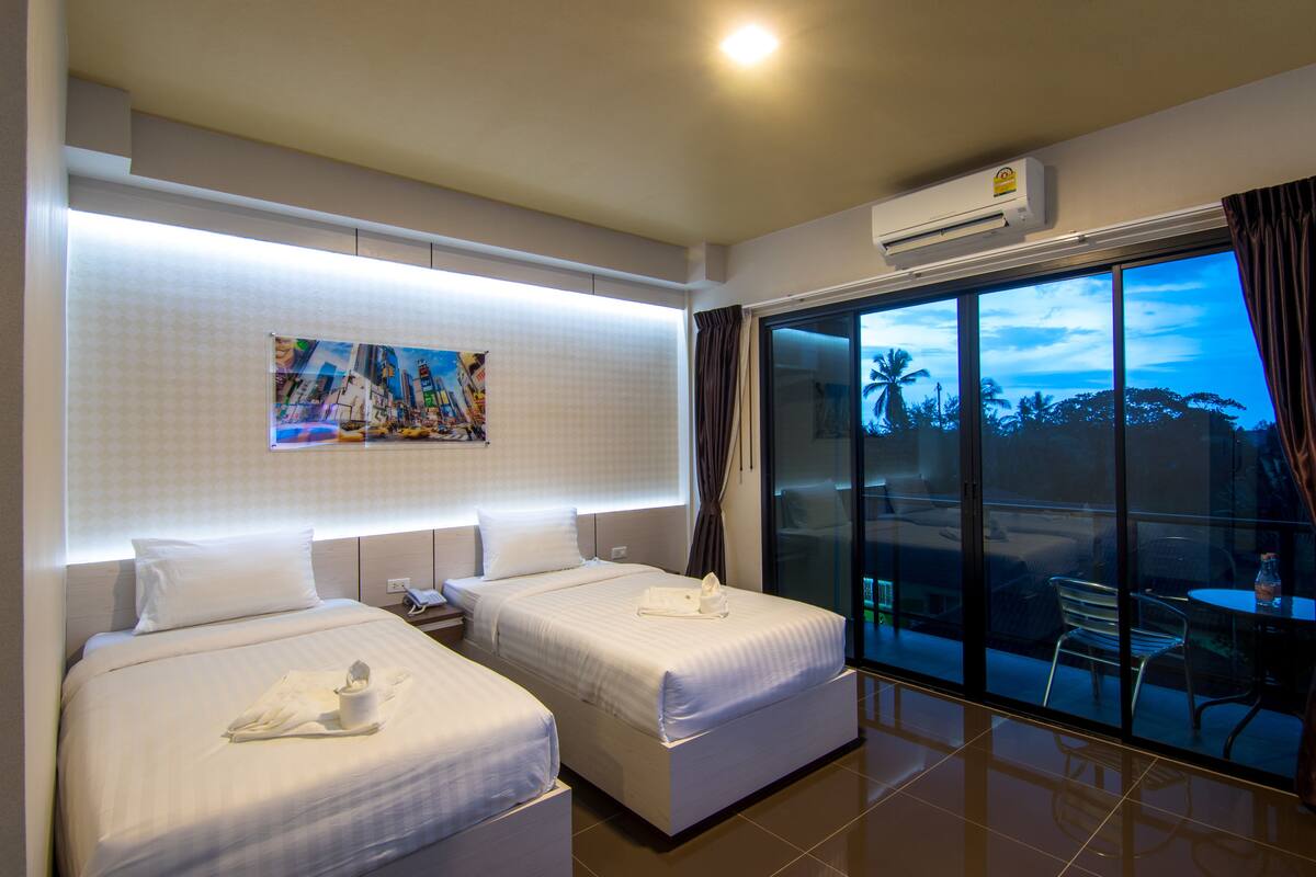 A hotel room with two beds, a large window with a view of palm trees, and a painting on the wall.