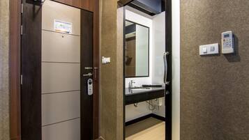 A hotel bathroom with a wooden door, a black sink, a mirror, and a wall-mounted thermostat.