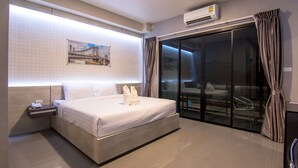 A modern hotel room with a large bed, a nightstand, a wall-mounted air conditioner, and a sliding glass door leading to a balcony. - PSG Hotel (Udon Thani)