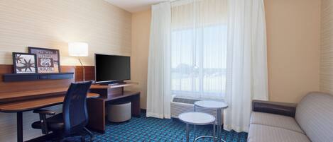 Une chambre d’hôtel équipée d’un bureau, d’une chaise, d’une télévision, d’un canapé et offrant une vue sur la ville grâce à de grandes fenêtres.