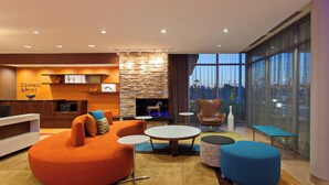 Una sala de estar moderna con chimenea de piedra, asientos naranja y azul, y vistas a la ciudad a través de amplios ventanales.