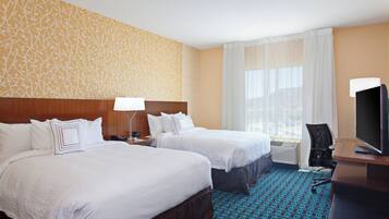 A hotel room with two beds, a desk with a television, and a large window with sheer curtains.