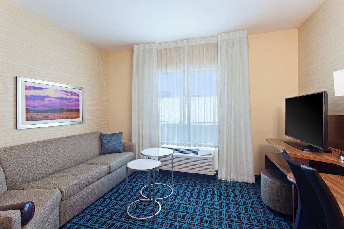 A hotel room with a sofa, a small round table, a television, and a window with curtains.
