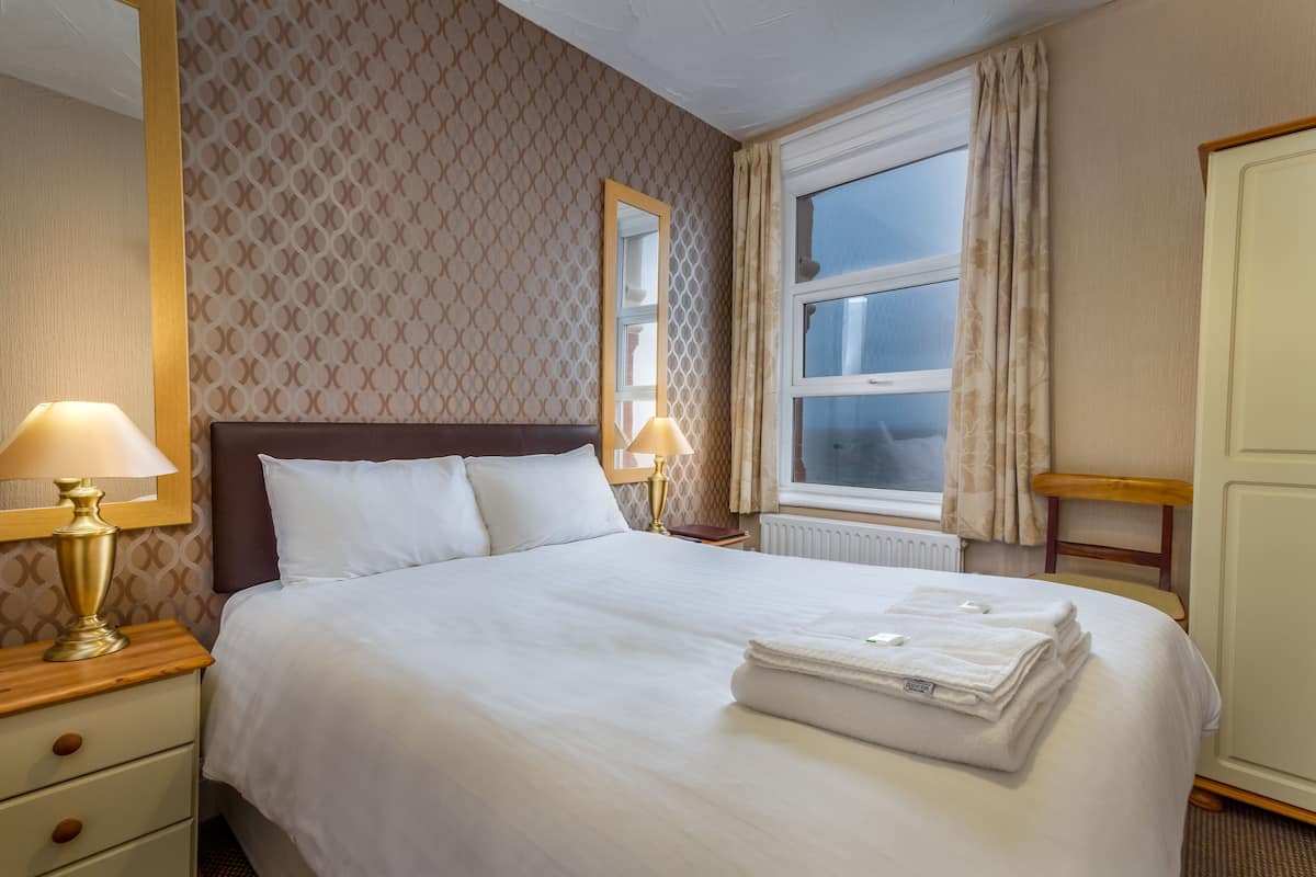 Cama bem arrumada com roupa branca, uma luminária de cabeceira e uma toalha dobrada na cama.