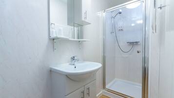 A modern bathroom with a white marble wall, a white sink with a mirror above it, and a glass-enclosed shower area.