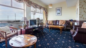 A room with a large window, a sofa, a table, and a TV. - The Maples Hotel (Blackpool)