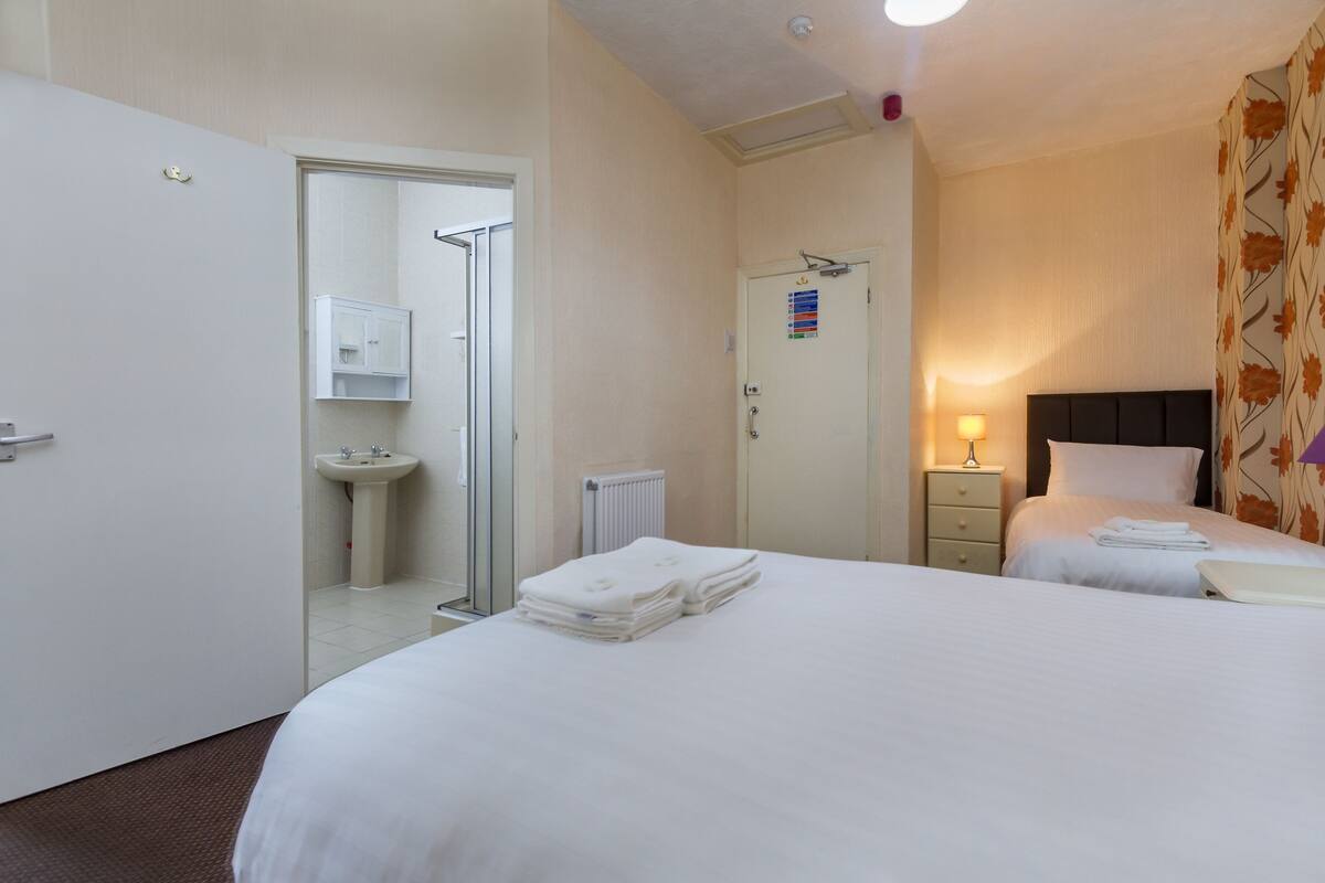 Quarto de hotel com duas camas, um banheiro e uma mesa de cabeceira com abajur.