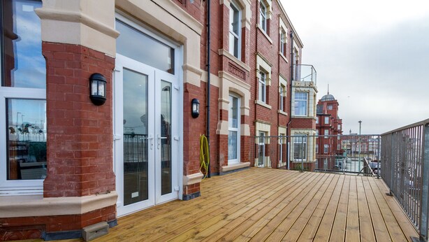 A wooden deck with a view of red brick buildings and a distant tower. - The Maples Hotel (Blackpool)
