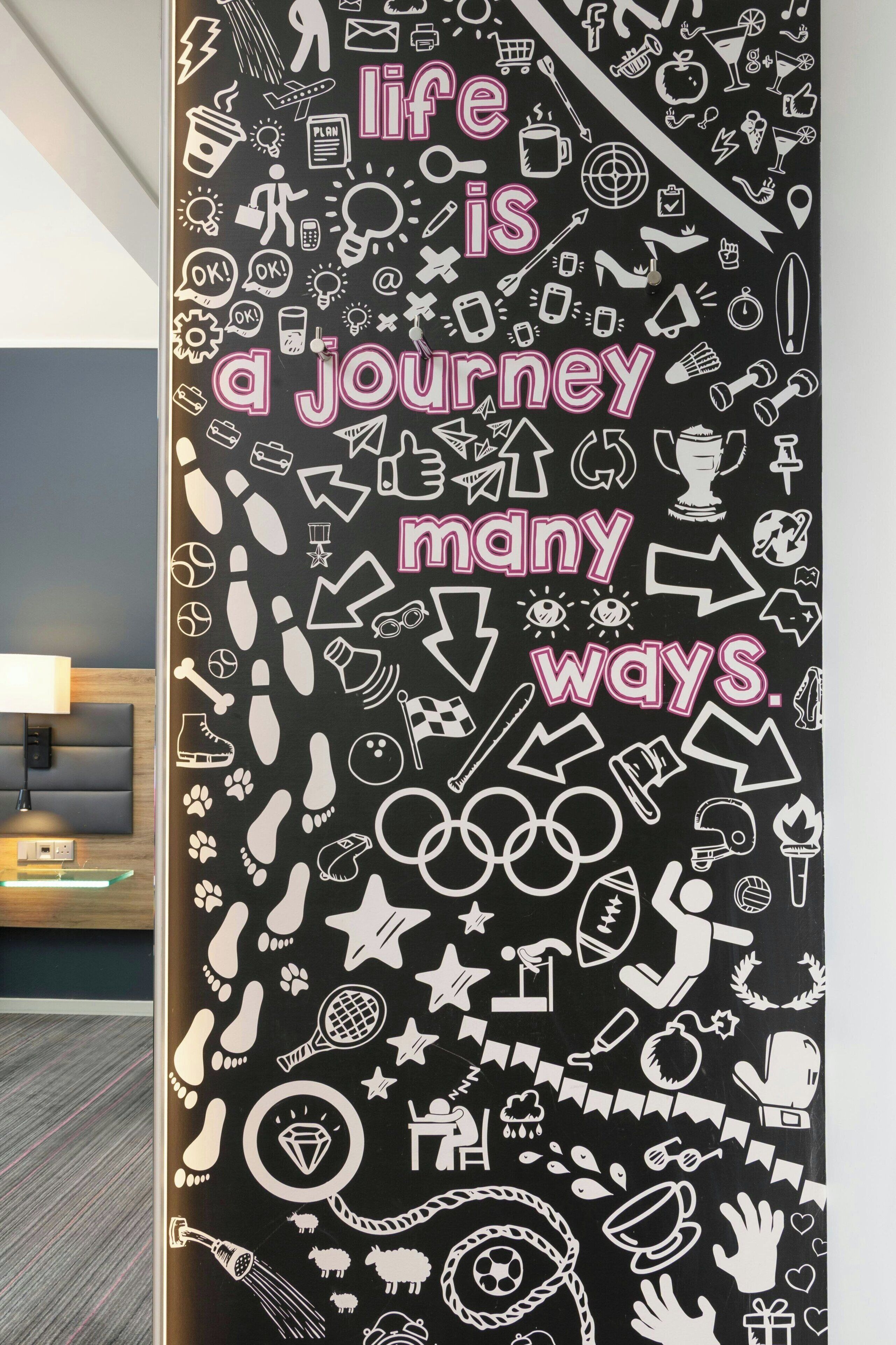 Un mur orné de divers pictogrammes et de textes, dont la phrase suivante : « La vie est un voyage, et il y a de nombreuses façons de la vivre. »