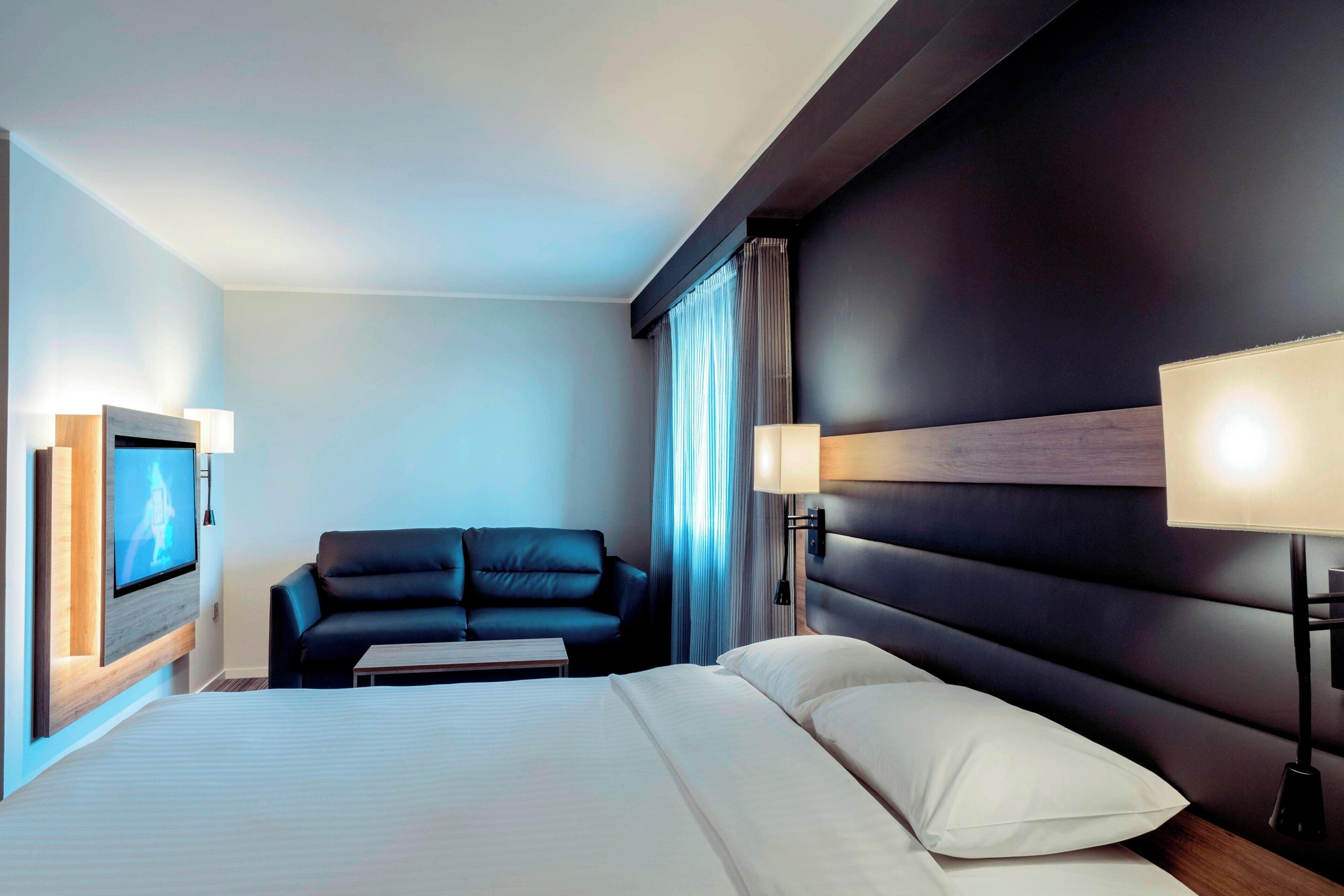 A hotel room with a bed, a sofa, a TV, and a lamp.