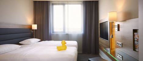 Une chambre d’hôtel avec deux lits, un téléviseur à écran plat, une lampe et une fenêtre avec des rideaux.