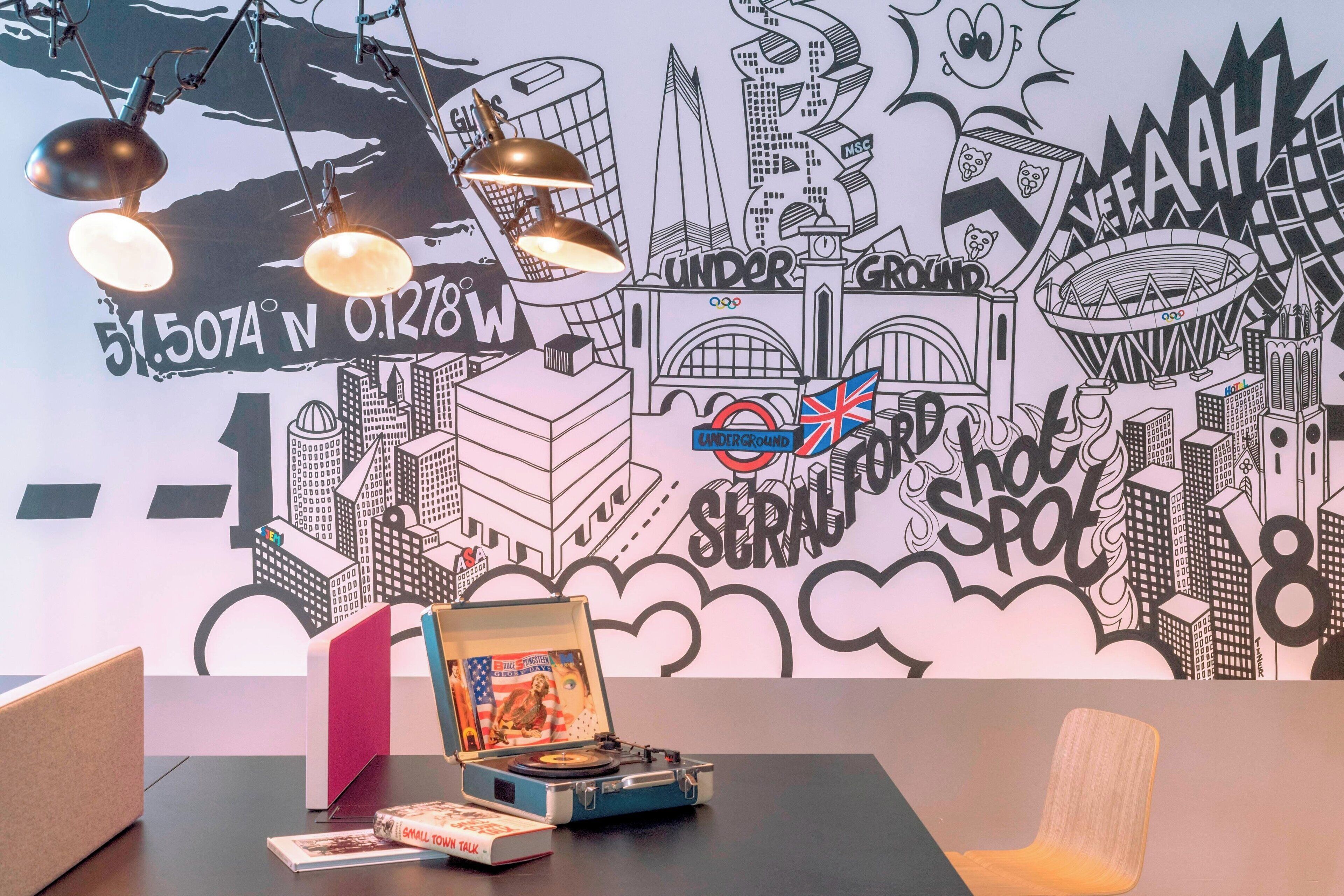A room with a wall mural of a cityscape, a turntable, and a small table with a book and a magazine.