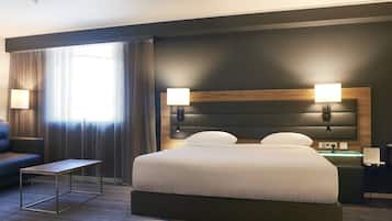 A modern hotel room with a large bed, bedside lamps, a small table, and a nightstand with a lamp.