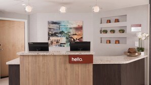 A reception desk with two monitors, a 'hello.' sign, and a cityscape painting above.