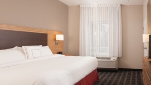 A hotel room with a large bed, a bedside table with a lamp, an air conditioning unit, and a window with curtains.