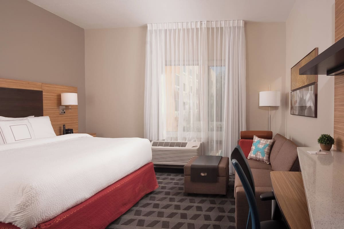 Une chambre d’hôtel avec un grand lit, un bureau, une chaise, un canapé et une fenêtre avec des rideaux légers.