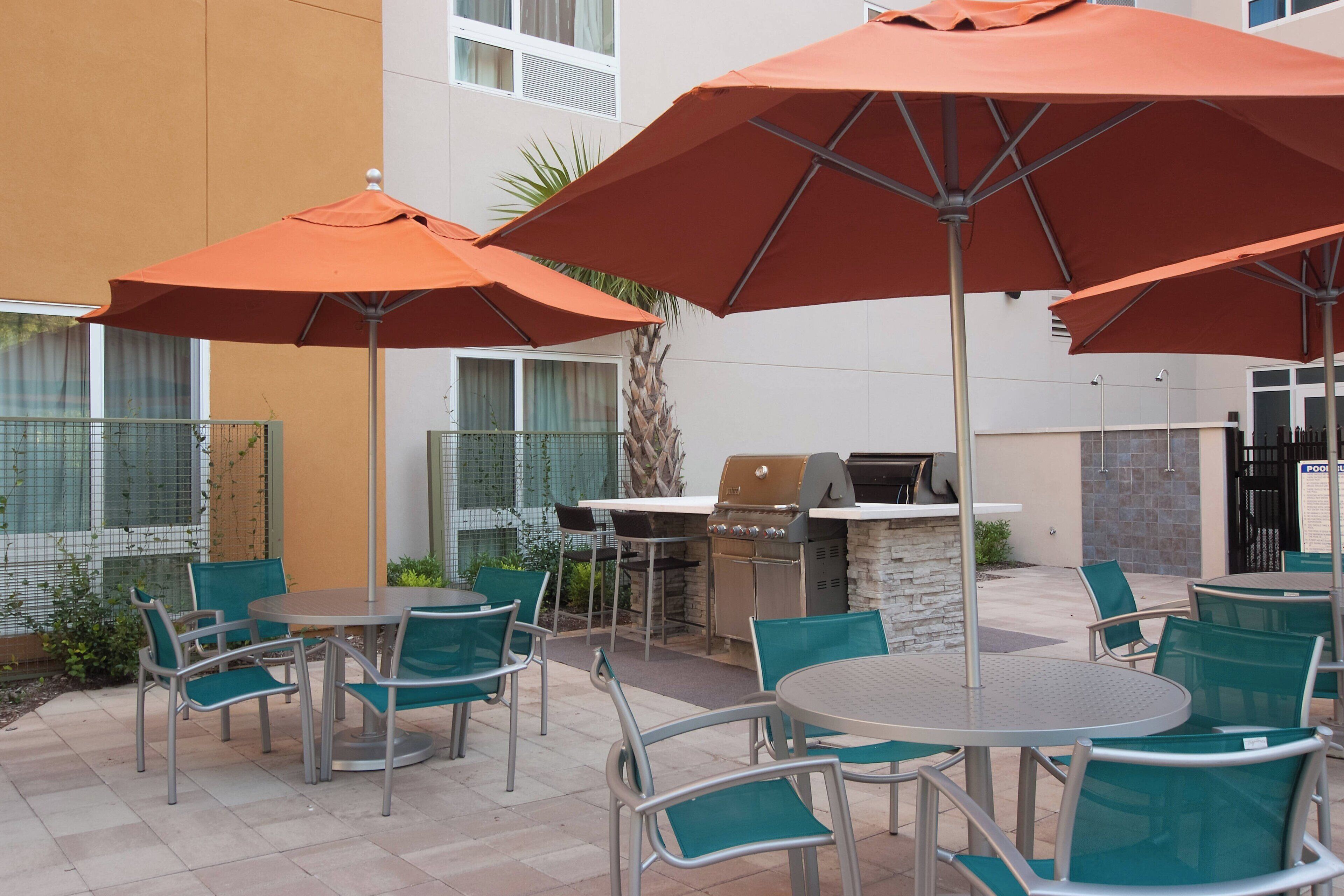 An outdoor patio with round tables and chairs, orange umbrellas, and a barbecue grill.