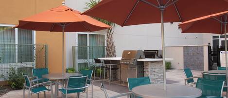 An outdoor patio with round tables and chairs, orange umbrellas, and a barbecue grill.
