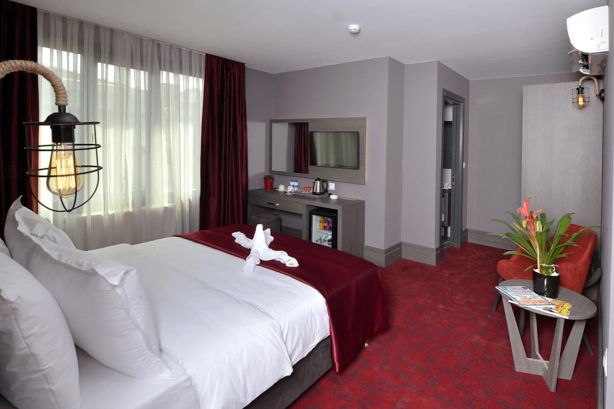 A hotel room with a bed, a desk, a mirror, and a red carpet.