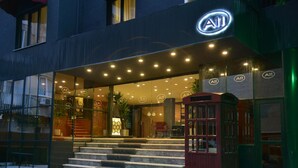 Entrada de hotel com design moderno, exibindo um logotipo A11 em destaque, um conjunto de degraus que levam à entrada e uma cabine telefônica vermelha.