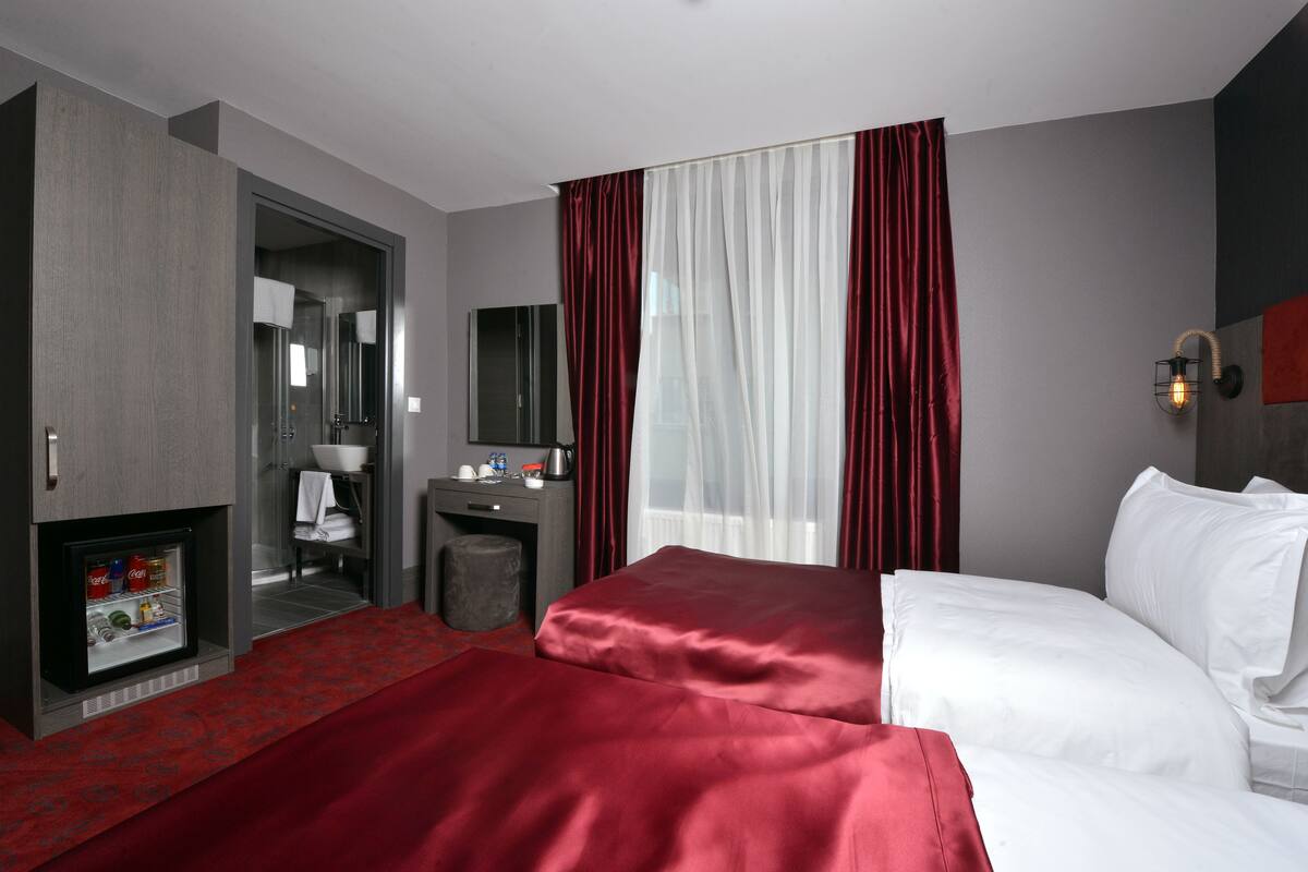 A hotel room with a bed, a desk, a mirror, a wardrobe, and a minibar.
