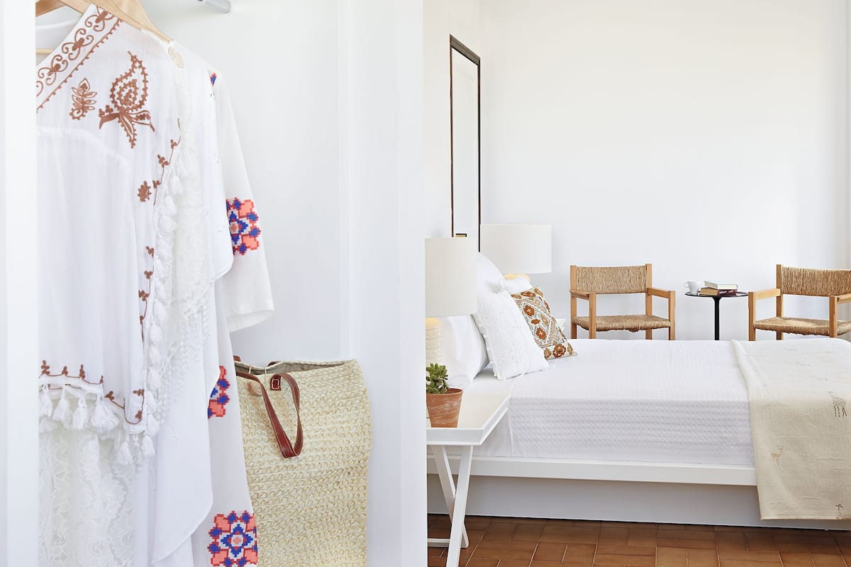 A bedroom with a bed, two chairs, a small table, and a hanging garment rack.