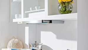 Una cocina moderna con encimera blanca, un lavamanos, una estufa y un estante sobre la encimera con un jarrón de flores amarillas.