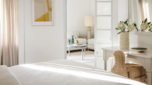 Habitación de hotel con cama, escritorio, silla, lámpara, un jarrón con flores y espejo.